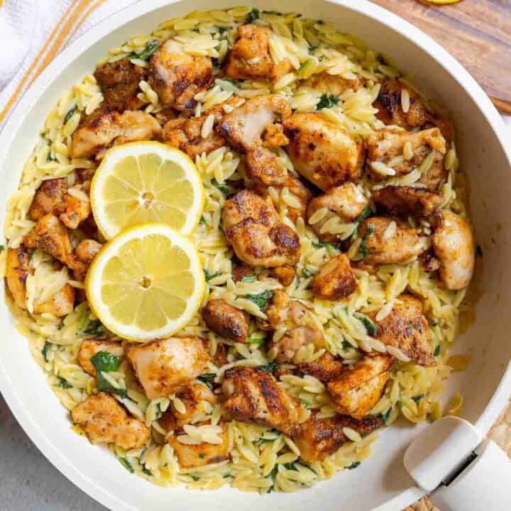 Lemon chicken orzo with diced chicken thighs and baby spinach in a large skillet.