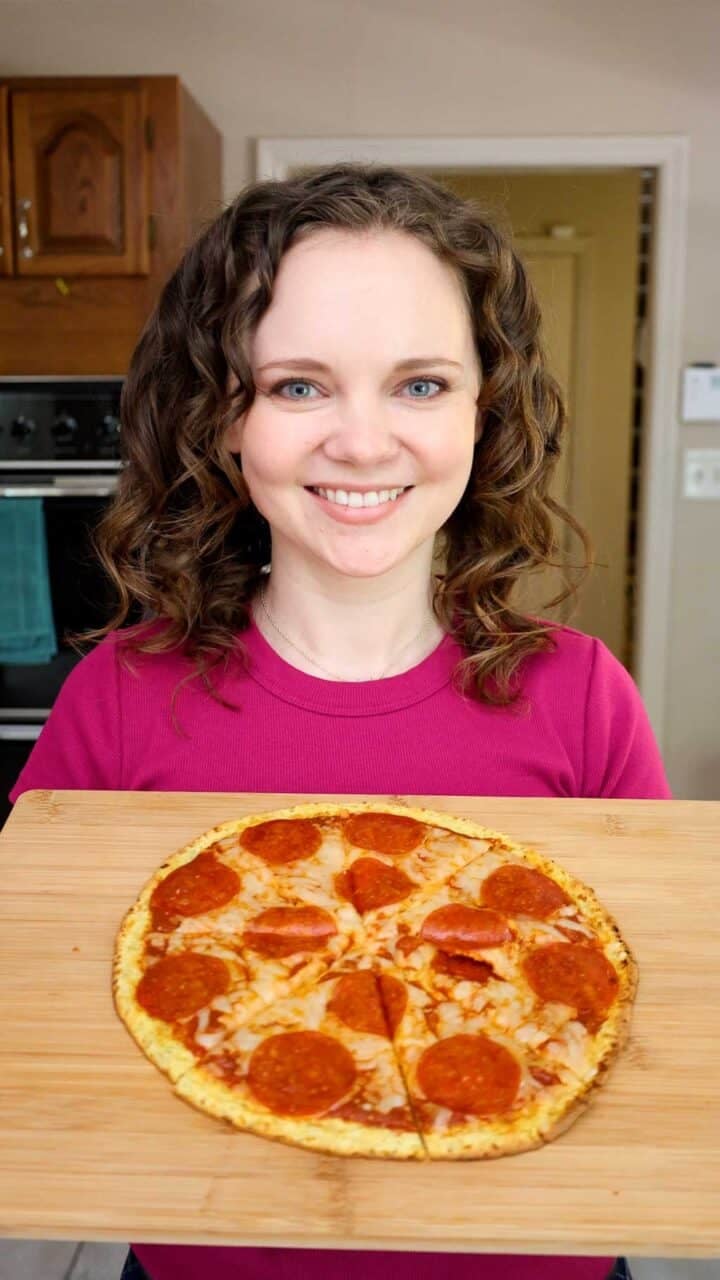 Kelsey Smith holding a cutting board with a pepperoni pizza on top.
