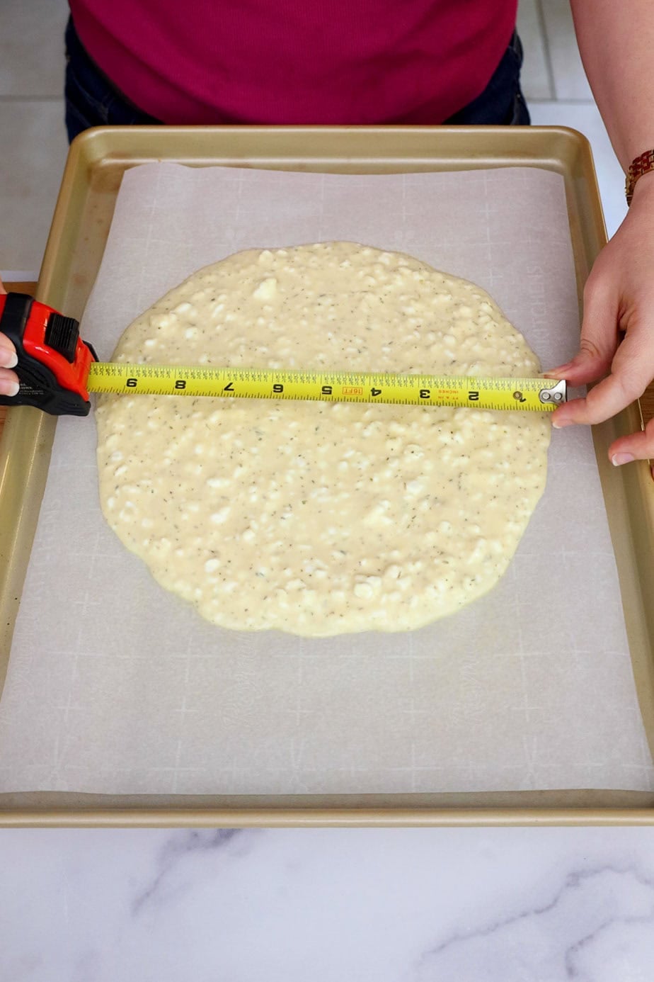 Batter spread into a circle on parchment paper with a tape measure showing the diameter of 10 inches.