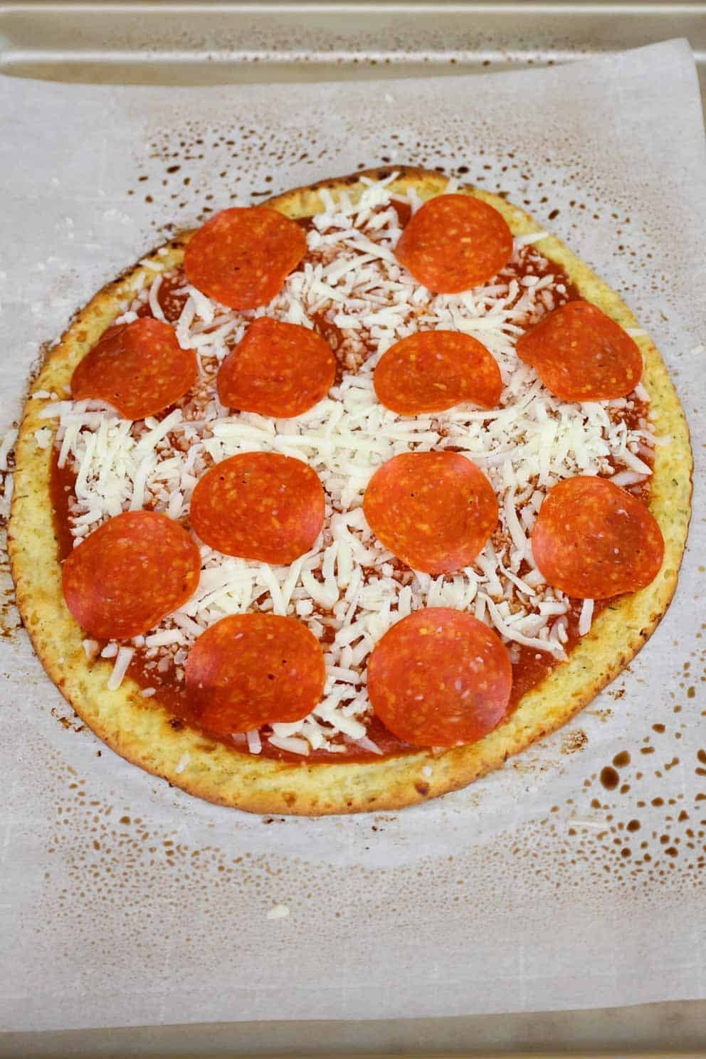 An unbaked pizza with sauce, shredded cheese, and pepperoni slices on top.