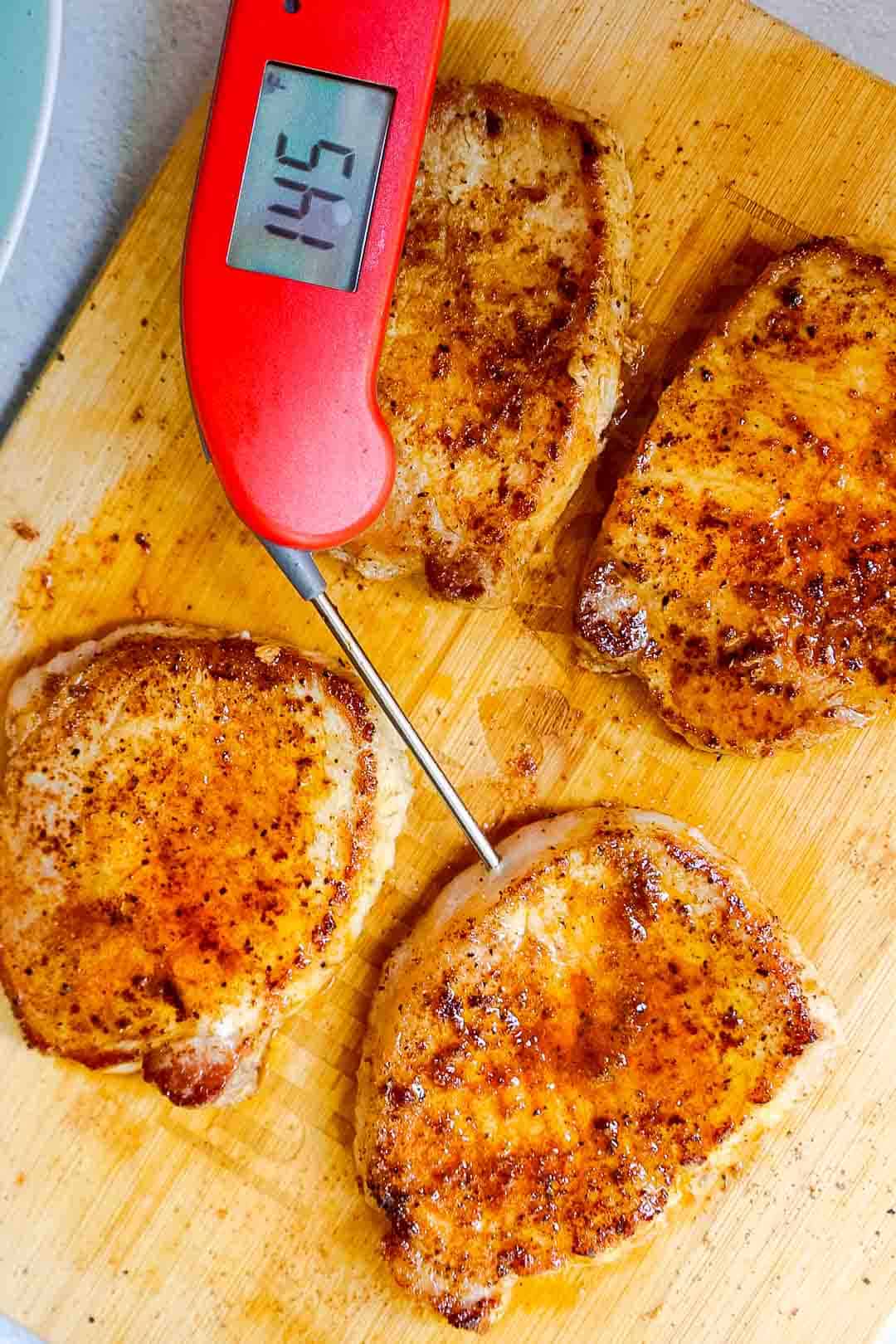 Cooked pork chops on a board with a meat thermometer reading 145°F.