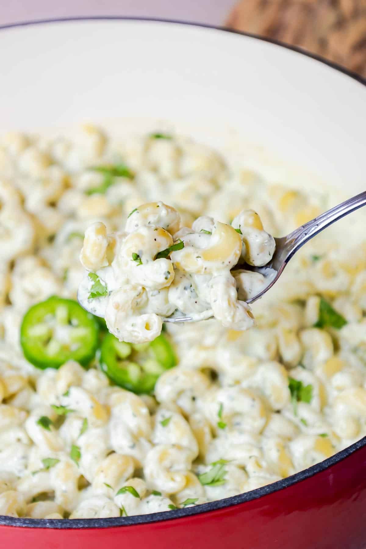 A spoon lifting creamy pasta from a pot with jalapeños and cilantro.