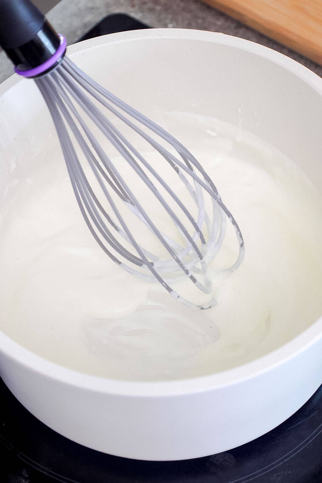 A whisk in a saucepan of white cream mixture.