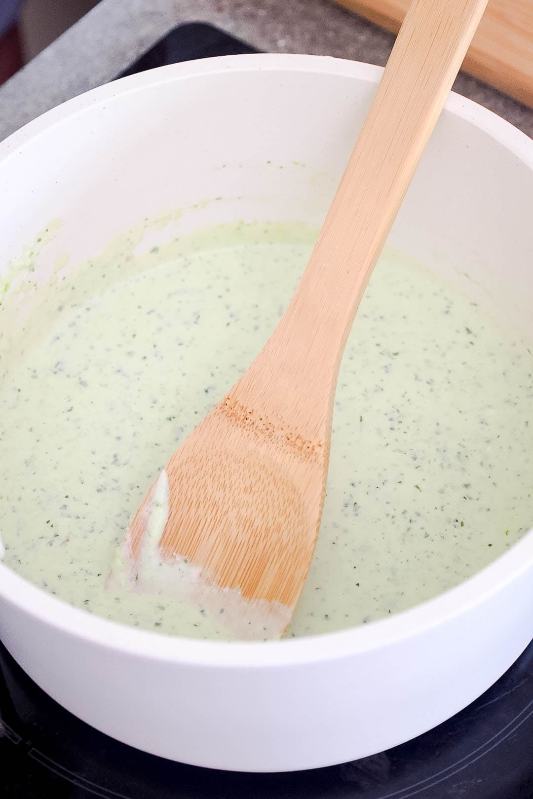 A saucepan with creamy jalapeño sauce and a wooden spoon.