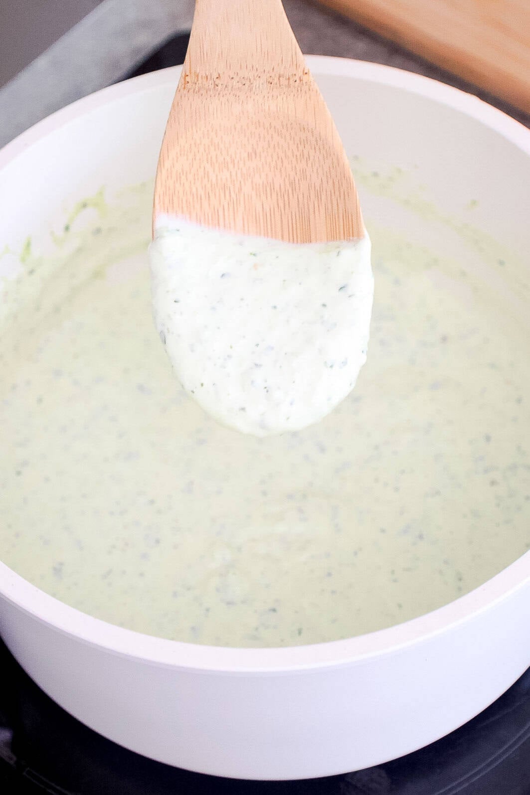 A spoon lifting thick and creamy jalapeño sauce from a saucepan.
