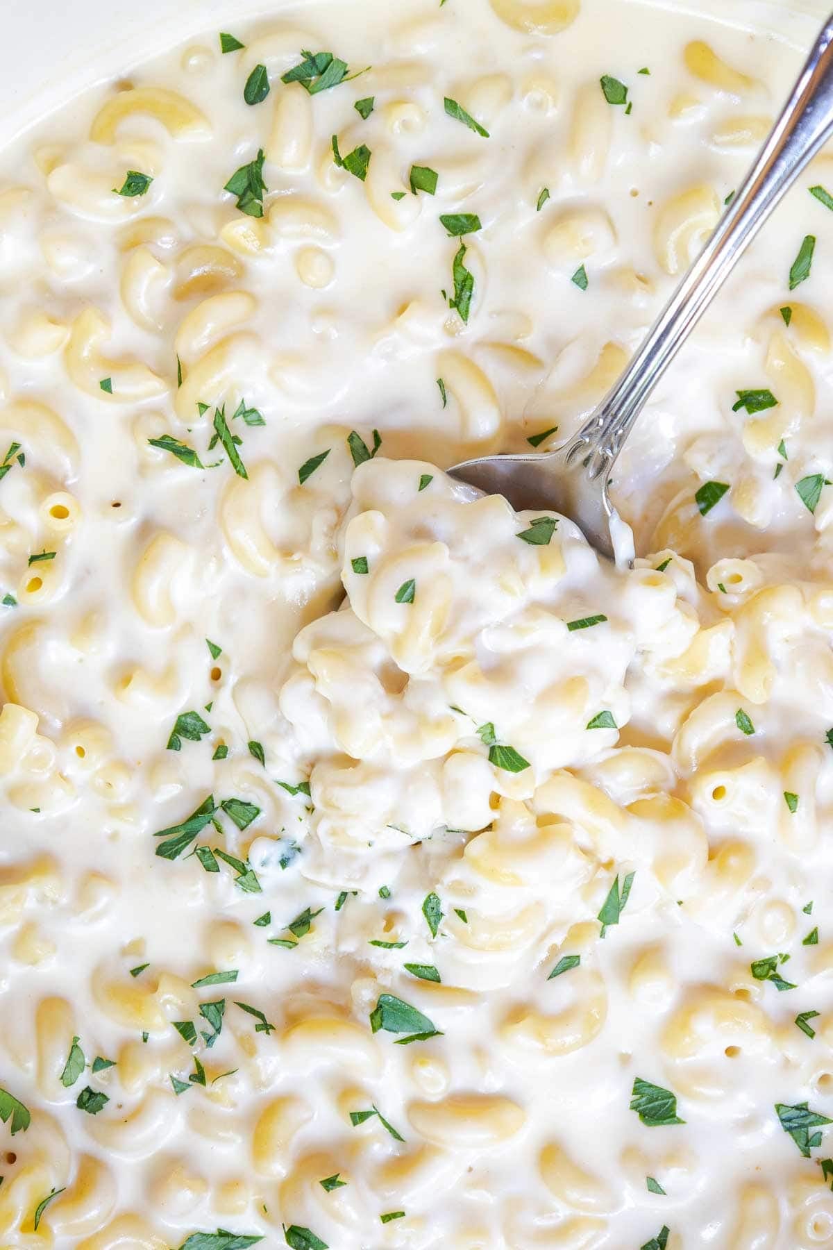 A spoon scooping white cheddar mac and cheese from a pot, garnished with parsley.