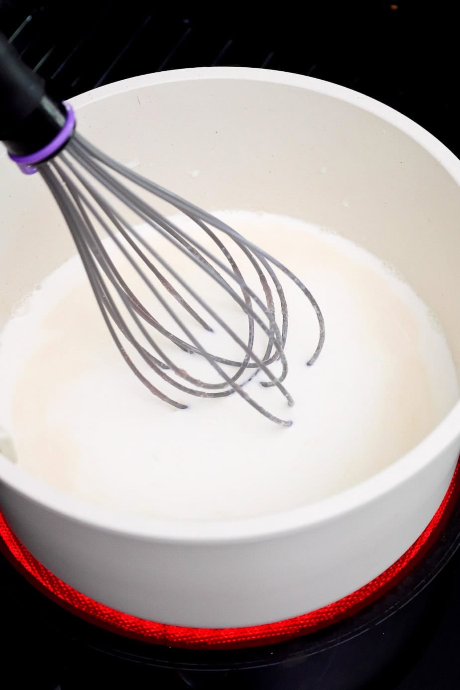 A whisk mixing half and half into the butter and flour mixture.