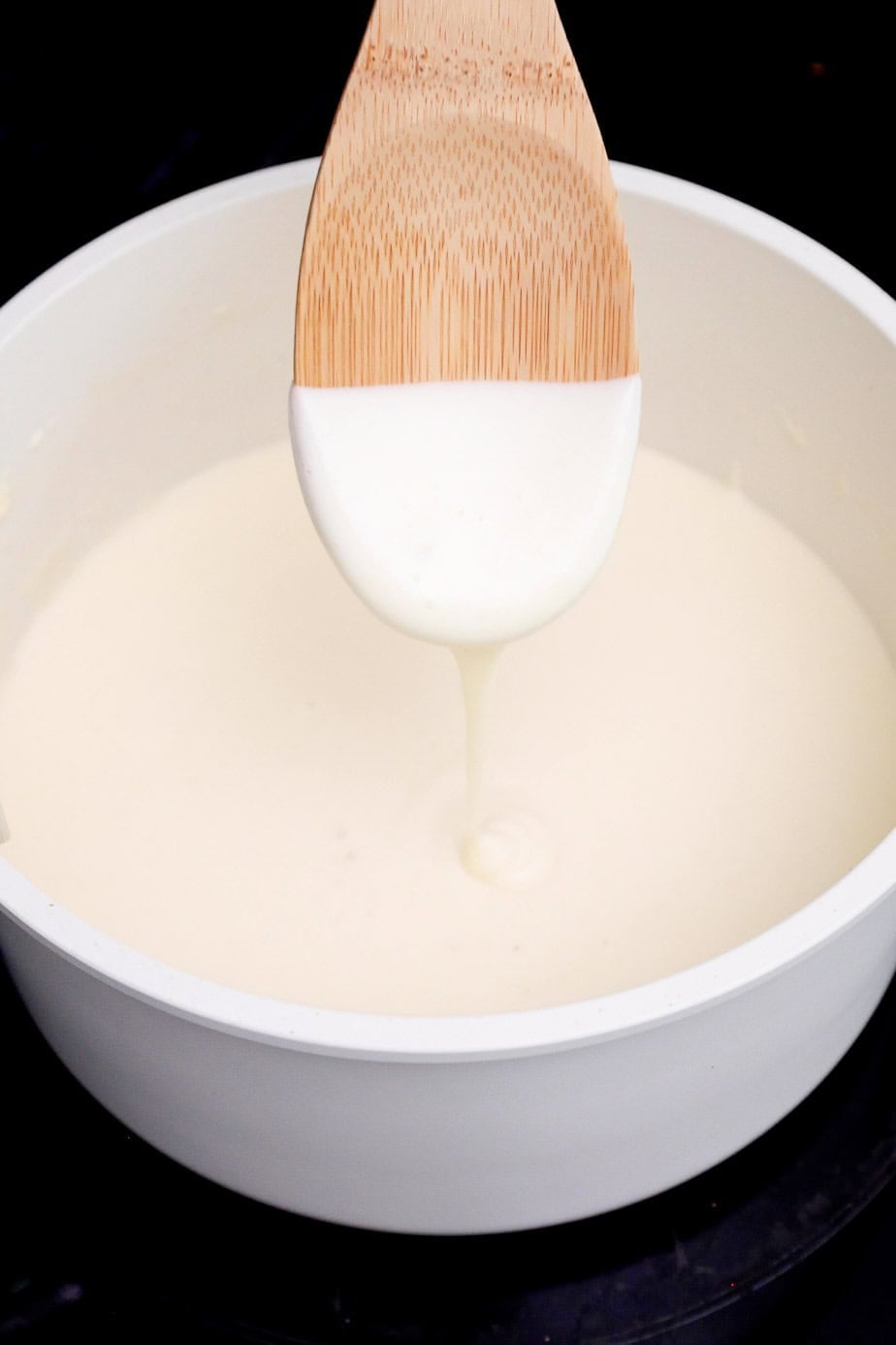 A spoon lifted from a pot of thickened cheese sauce.