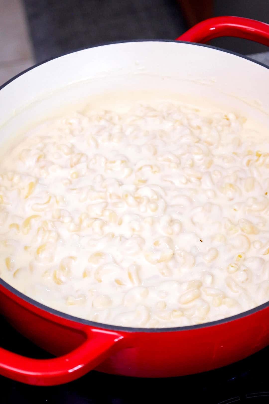 Cooked elbow macaroni in a large pot coated with cheese sauce.