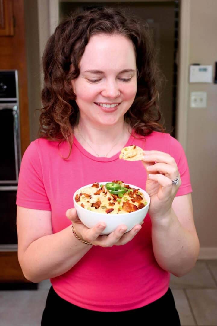 Kelsey Smith holding a bowl of jalapeño popper dip and looking at a chip scooped into the dip.