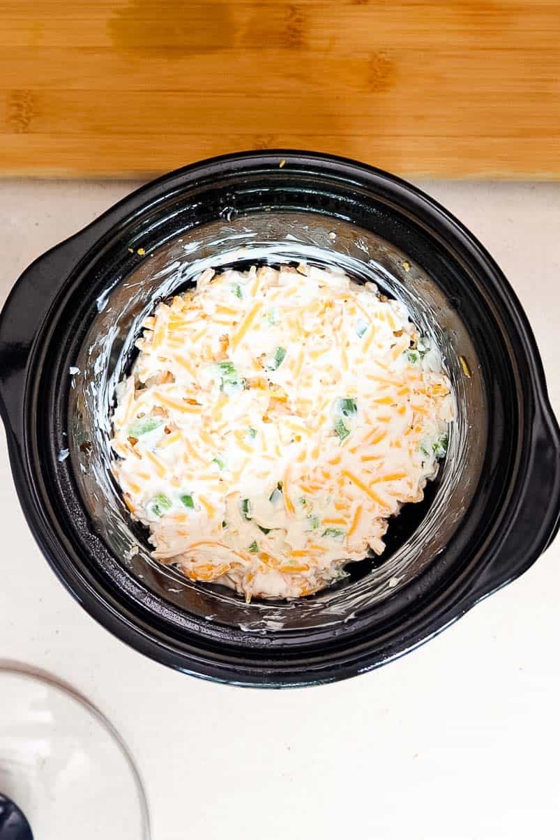 Softened cream cheese, sour cream, garlic powder, diced jalapeños, and shredded cheddar mixed together in a small Crockpot.
