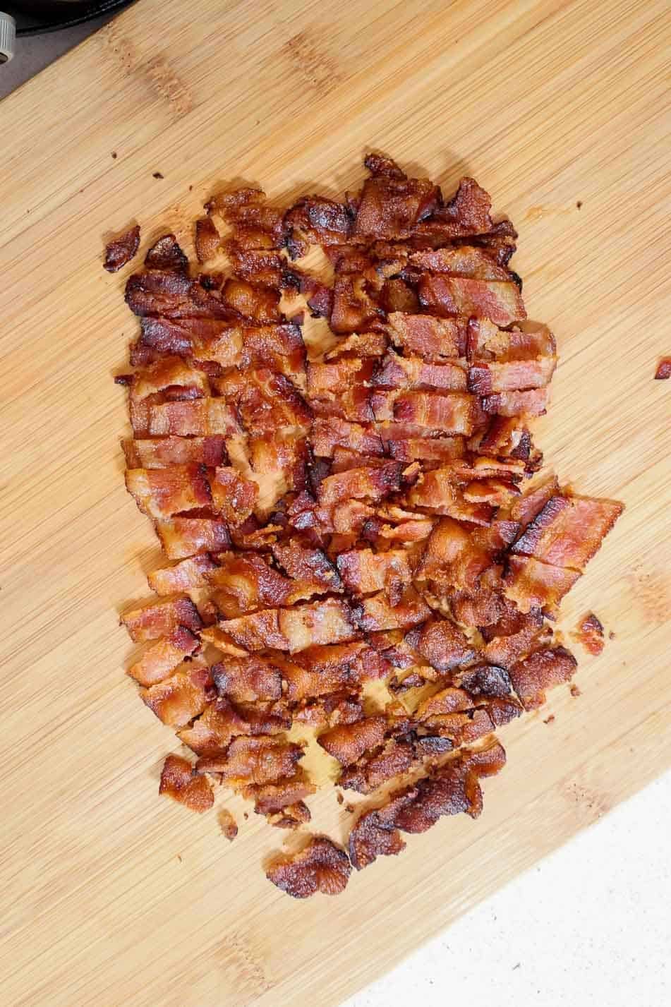 Chopped crispy bacon pieces on a wooden cutting board.