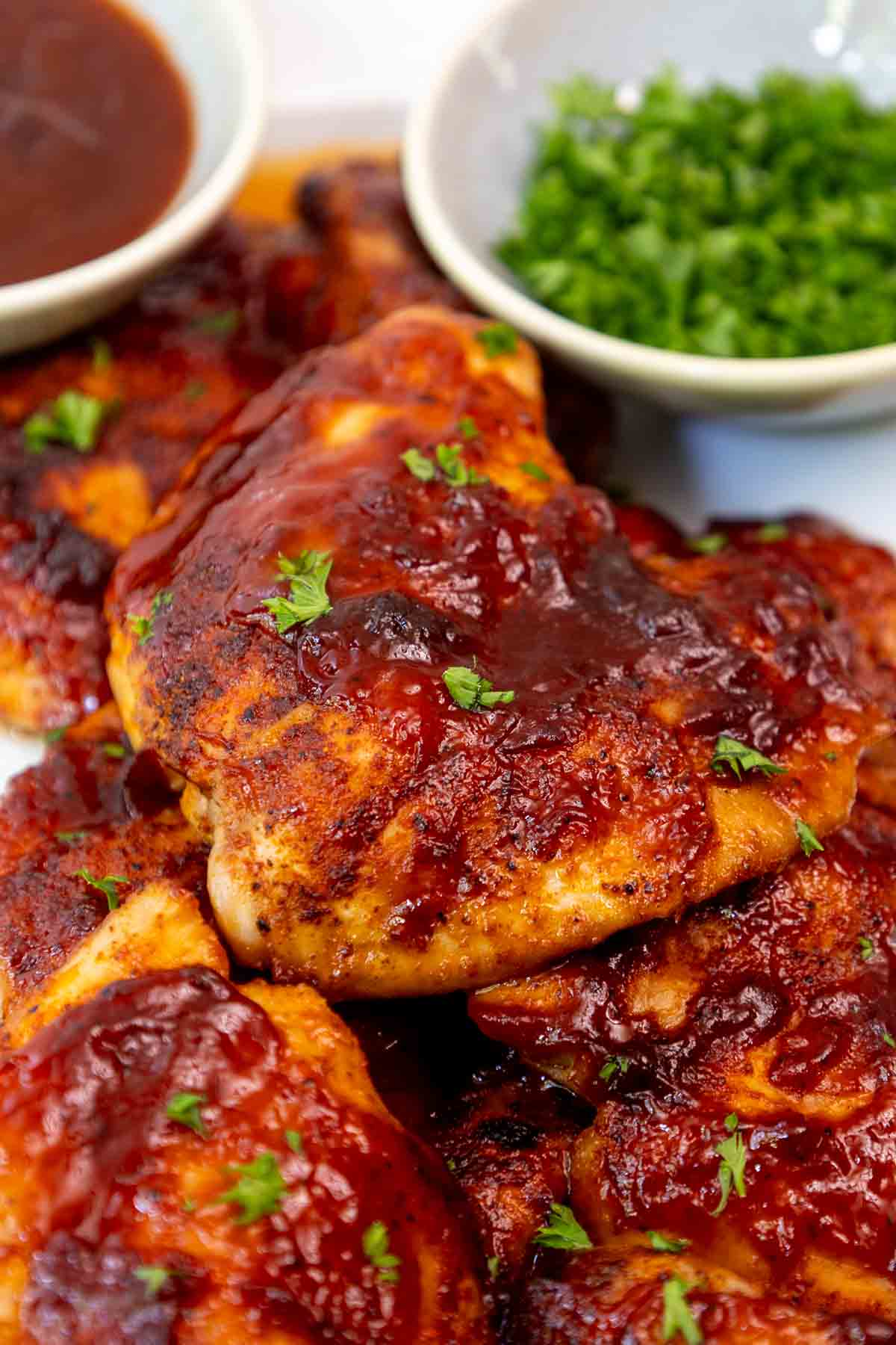 Pile of juicy oven baked BBQ boneless chicken thighs on a serving platter garnished with chopped parsley.