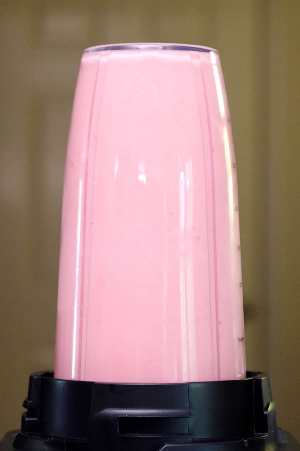 A pink strawberry smoothie blending in a clear blender cup.