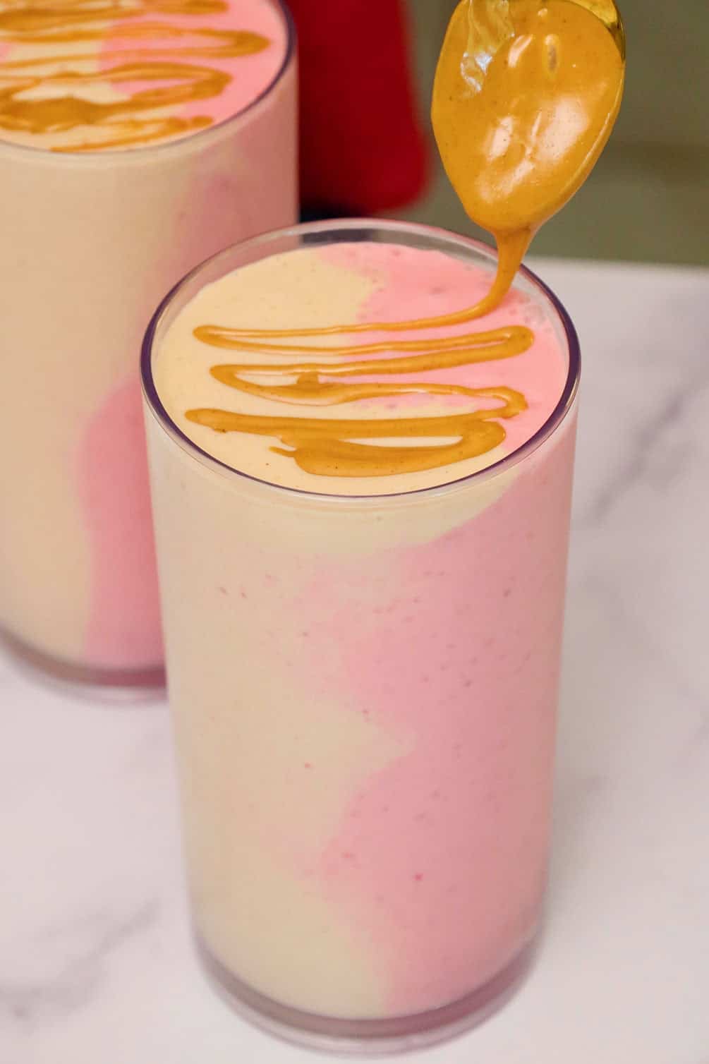 Peanut butter being drizzled over the top of a finished swirled peanut butter and jelly smoothie in a glass.