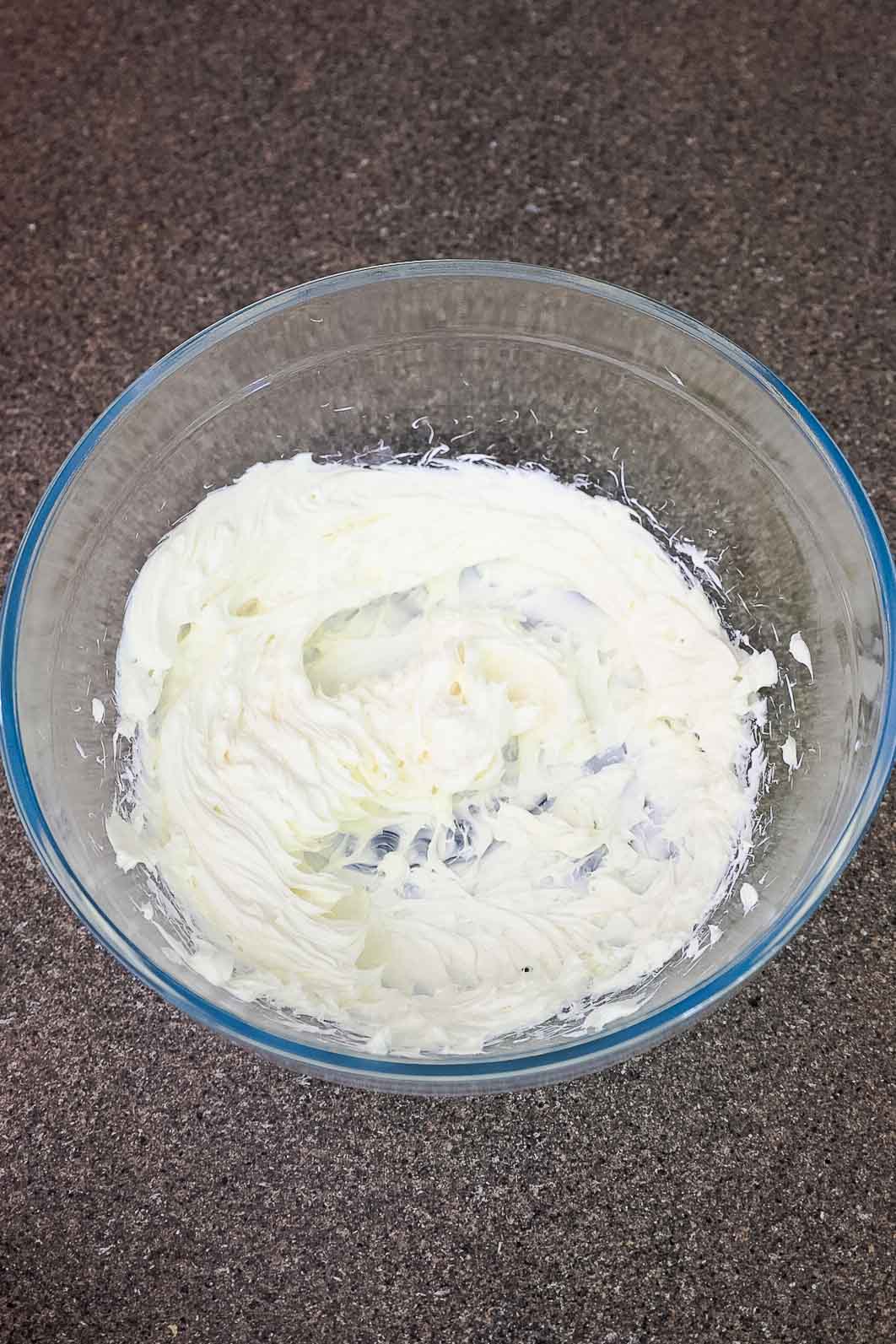 Cream cheese whipped in a glass mixing bowl.