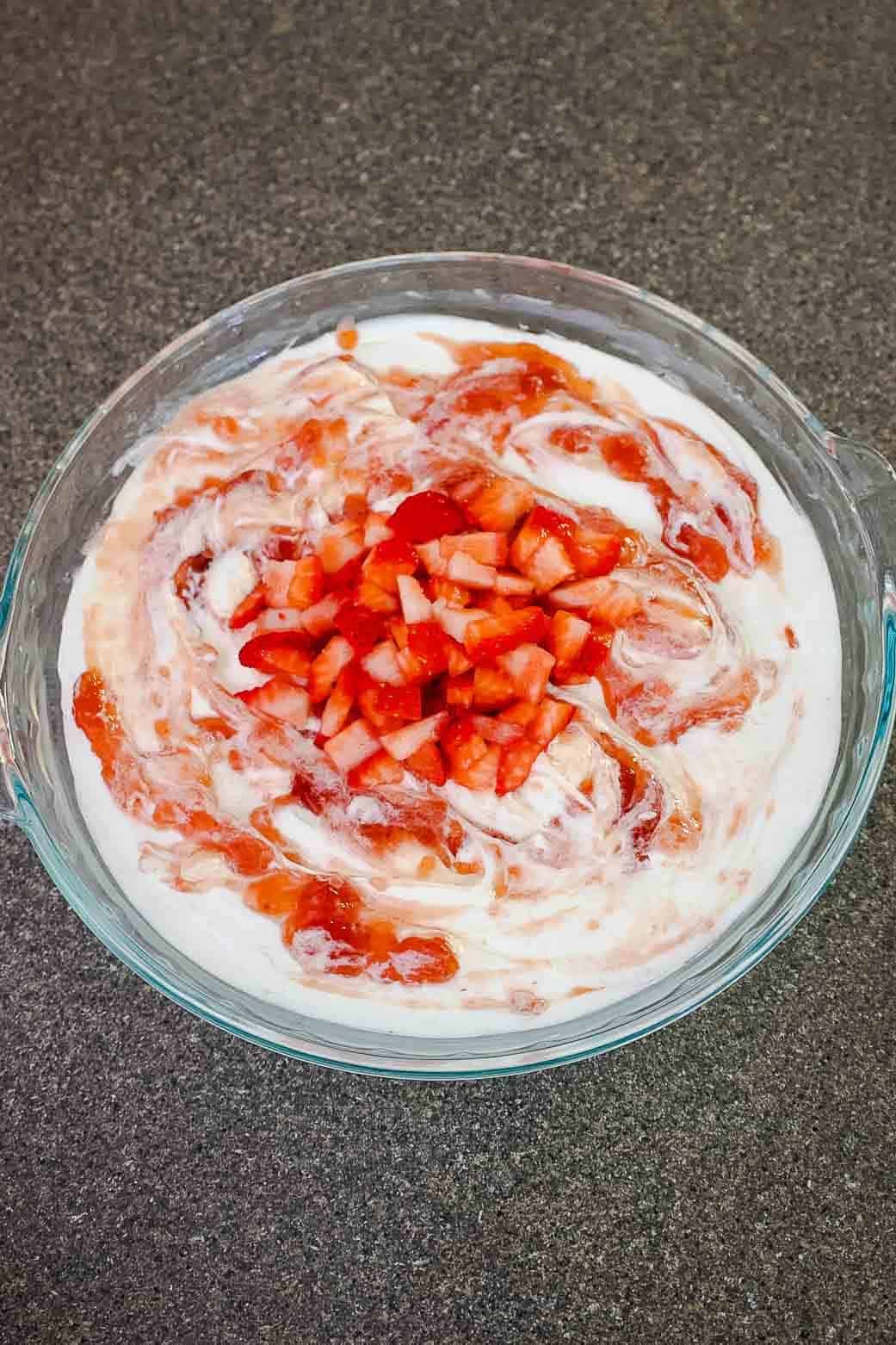 Finished dessert dip with strawberry jam swirls and a generous topping of diced strawberries in the center.