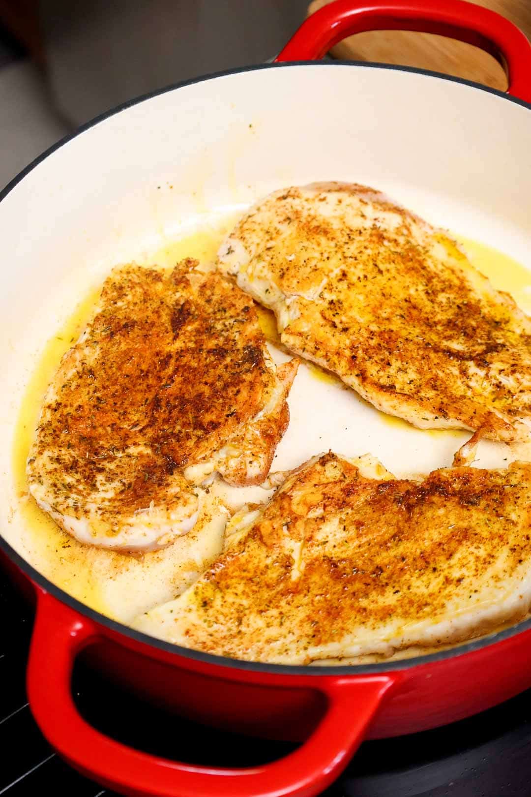 Seasoned chicken breasts searing in olive oil inside a Dutch oven, developing a golden brown crust.