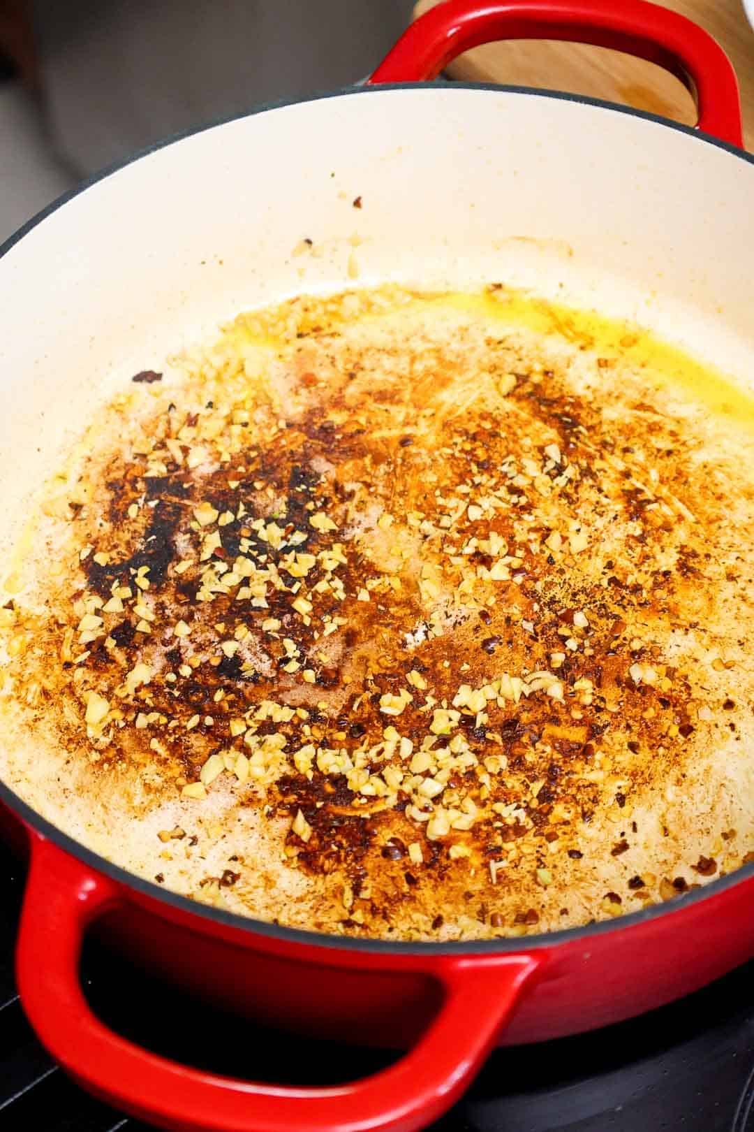 Minced garlic and red pepper flakes sautéing in the browned bits left behind in a red Dutch oven.