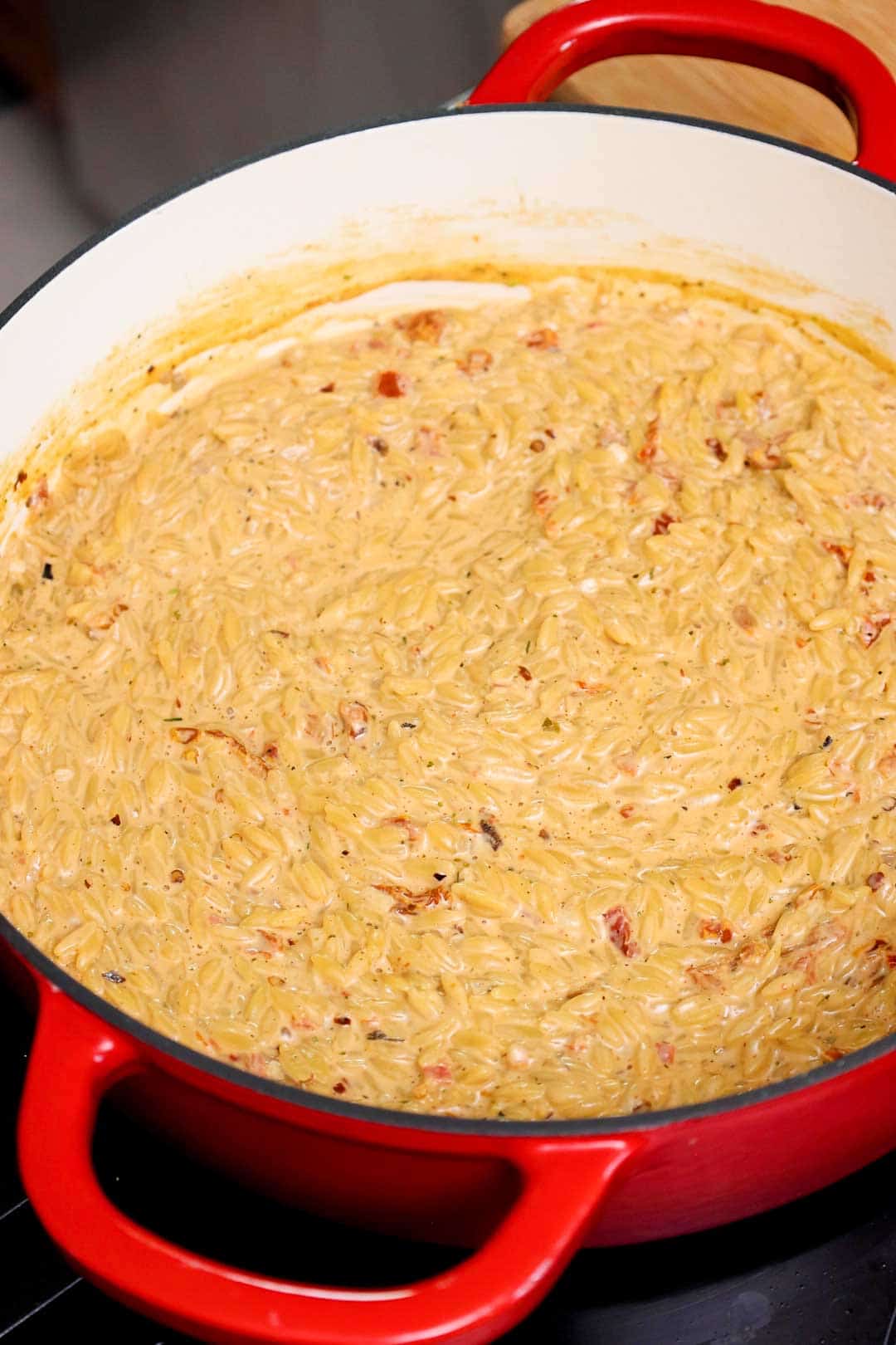 Creamy orzo with visible bits of sun-dried tomato thickening in a Dutch oven.