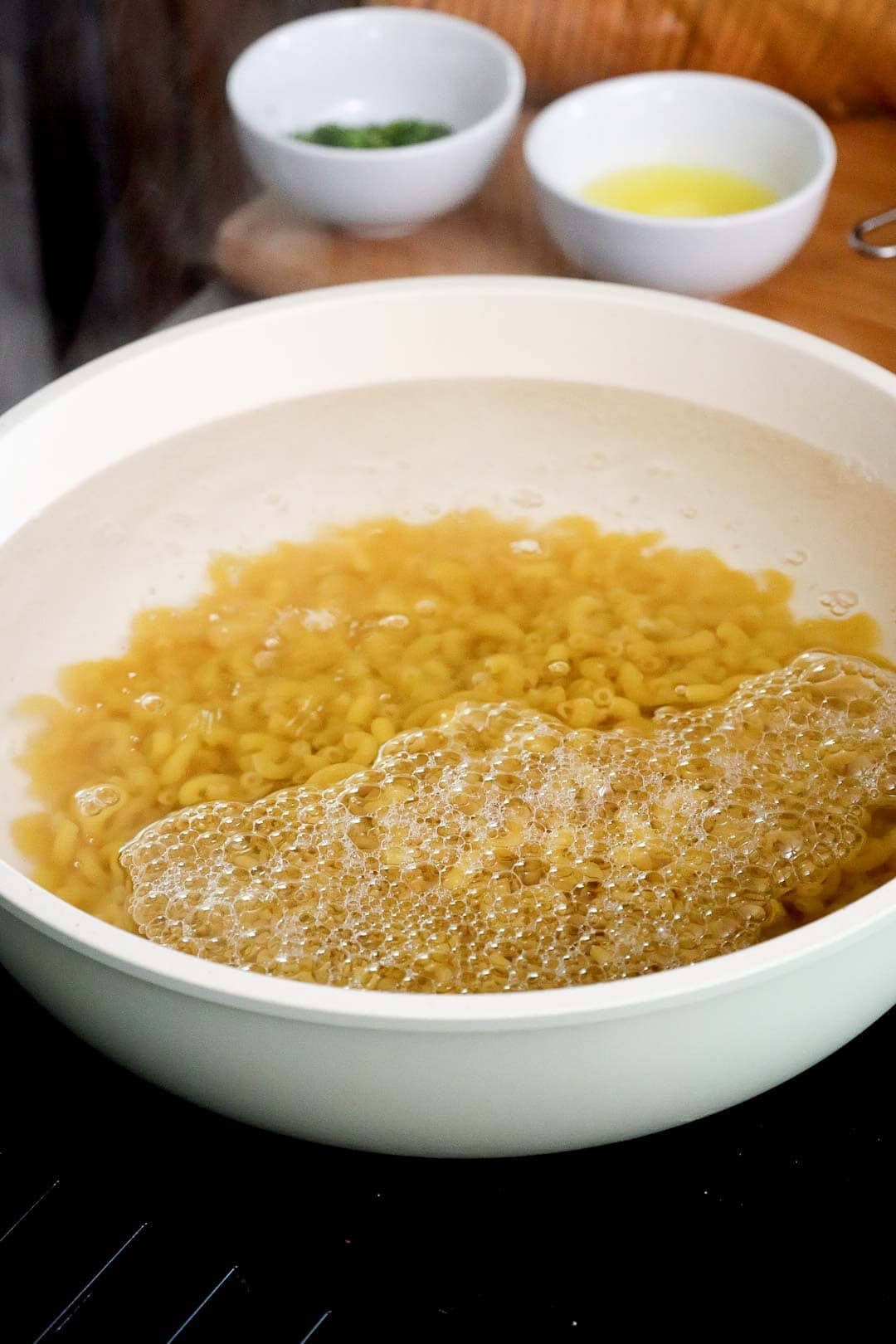 Elbow macaroni boiling in a large white pot of bubbling water.