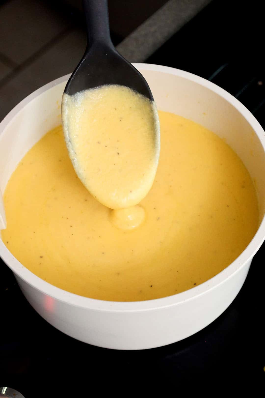 Thick, creamy cheese sauce made from shredded cheddar and milk being stirred with a spoon in a saucepan.