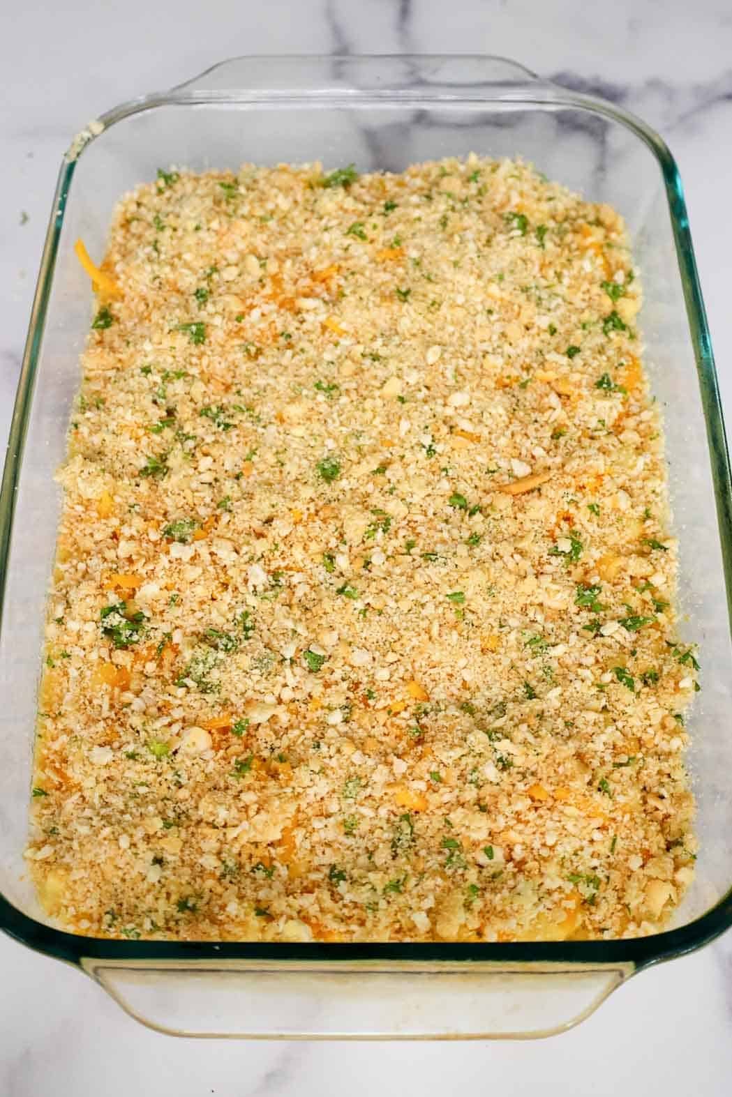 Casserole dish of mac and cheese fully layered with crushed Ritz crackers and parsley, prepped and ready for baking.