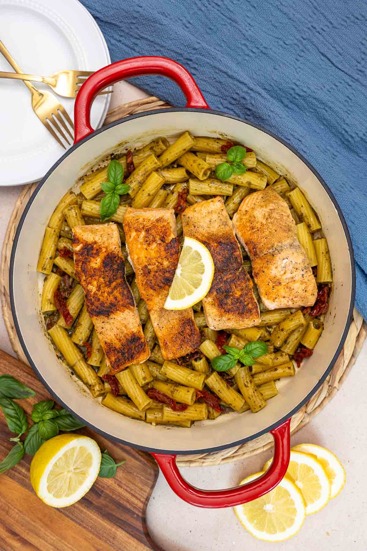 Top-down view of pot filled with salmon pesto pasta topped with four seared salmon fillet on top of rigatoni with sun-dried tomatoes.