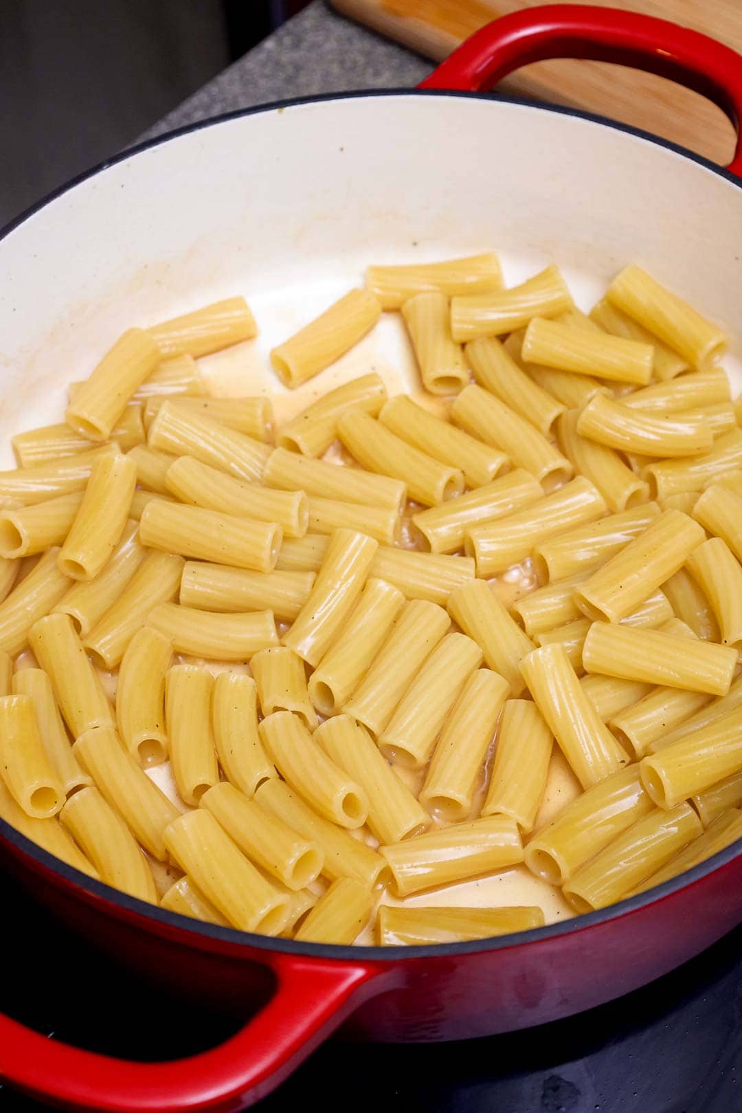 Uncooked rigatoni pasta added to the Dutch oven with chicken broth.