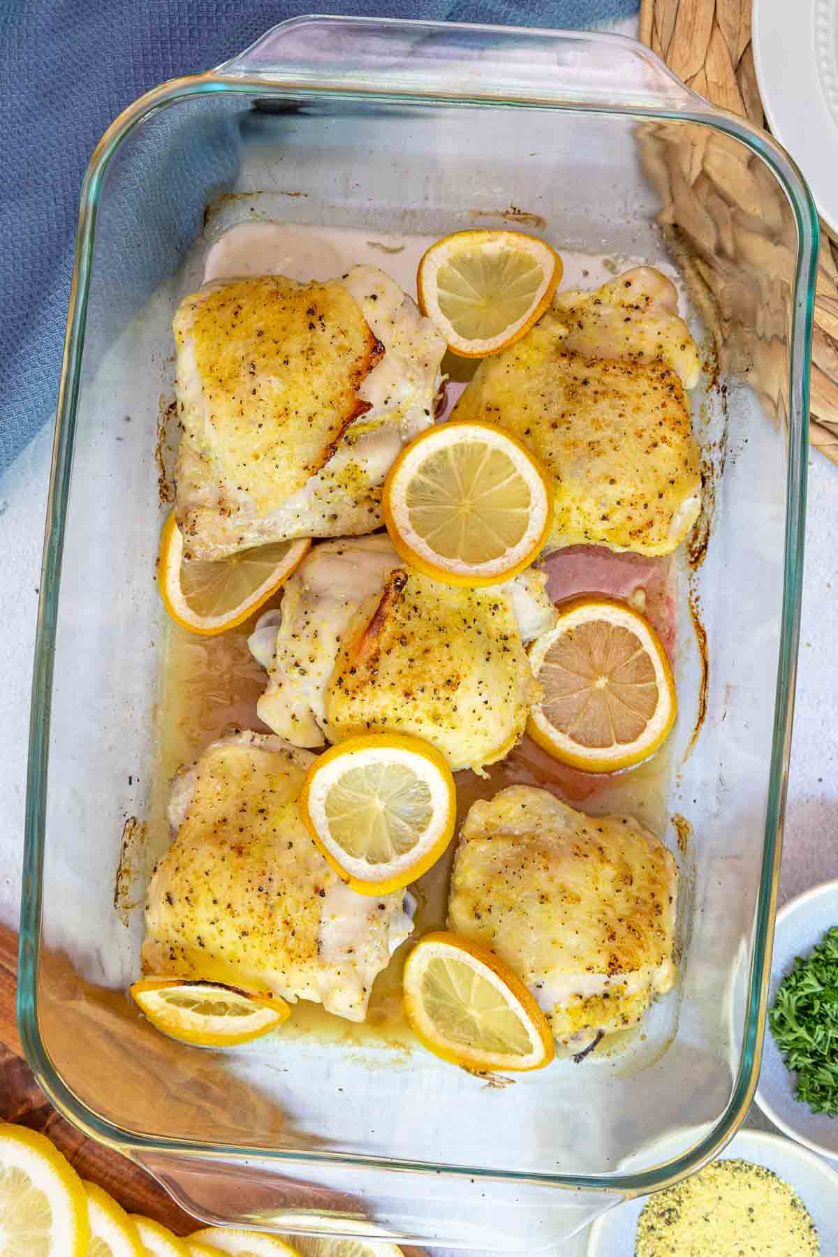 Cooked lemon pepper chicken thighs fresh out of the oven in a glass baking dish, surrounded by roasted lemon slices and pan juices.