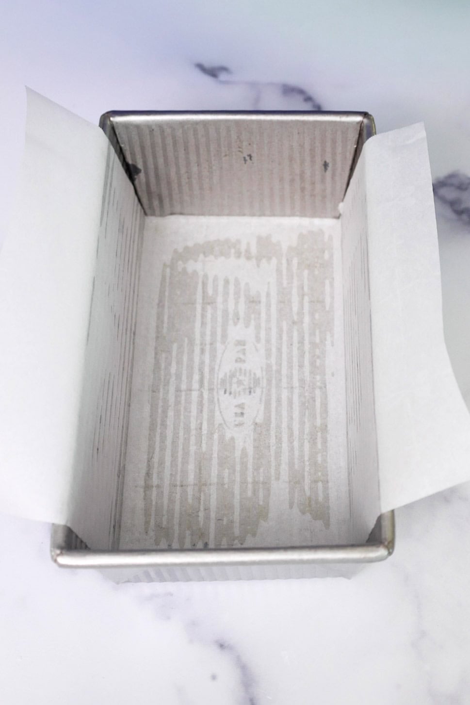 An empty loaf pan greased with cooking spray and lined with parchment paper, ready for batter.