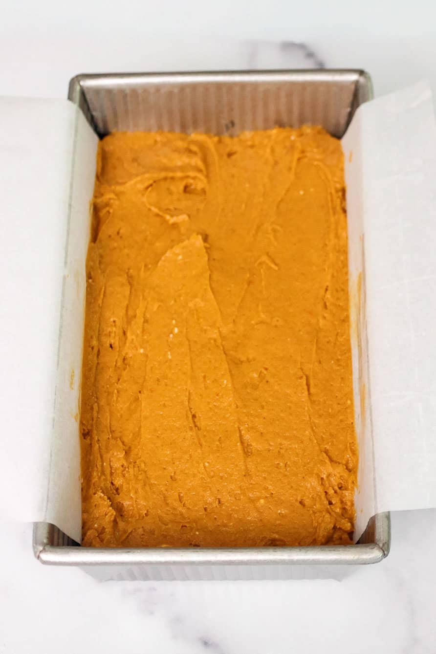 Pumpkin bread batter smoothed into a parchment-lined loaf pan, ready to bake.
