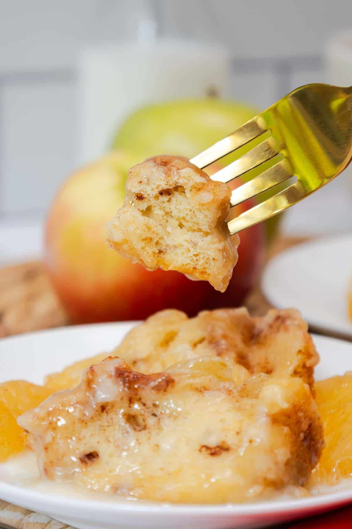 A bite of cinnamon roll bake on a fork held over a plated serving.