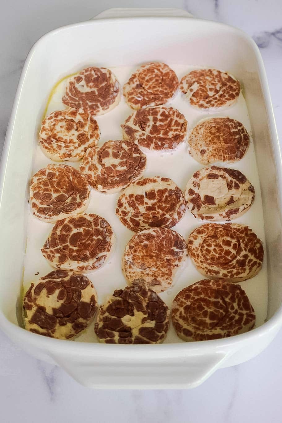 Cinnamon roll pieces arranged in a baking dish cinnamon side up.