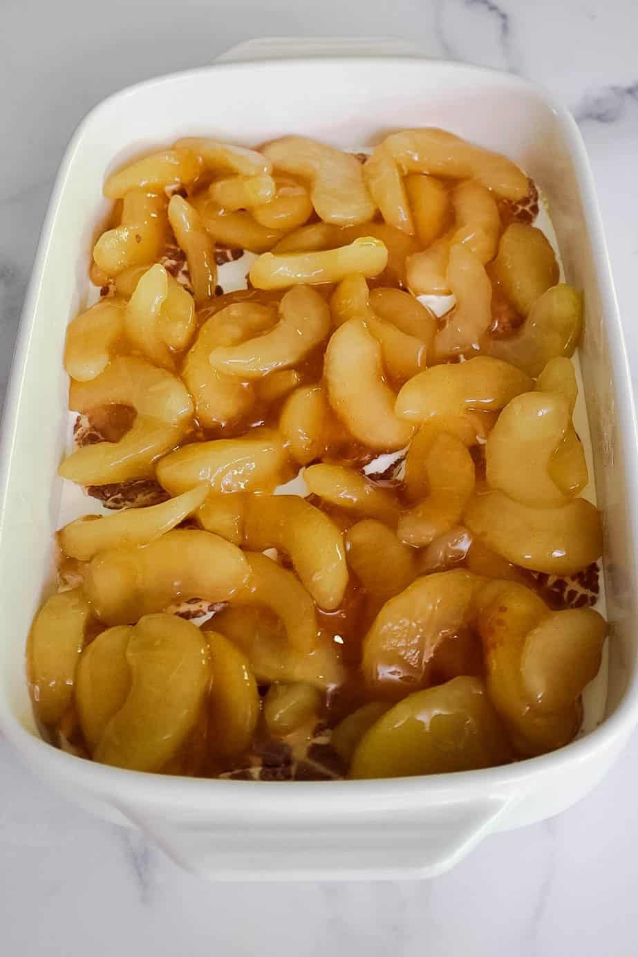 Apple pie filling layered over cinnamon roll dough in a baking dish.