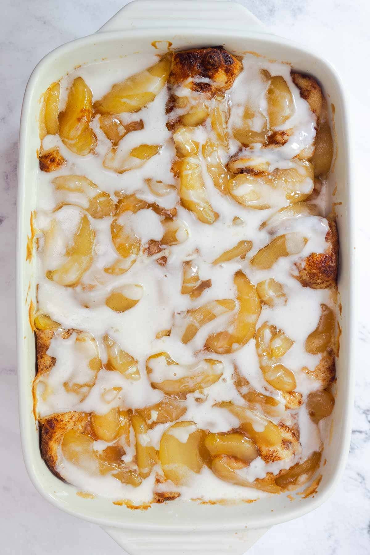 Baked cinnamon roll casserole covered in icing and apple pie filling.