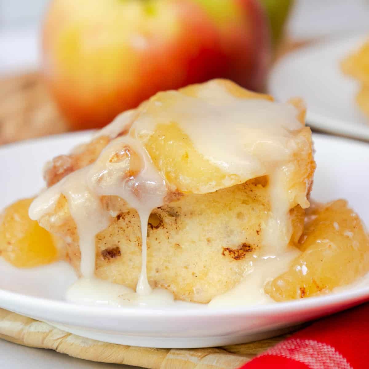 A cinnamon roll on a plate topped with apple pie filling and dripping with icing.
