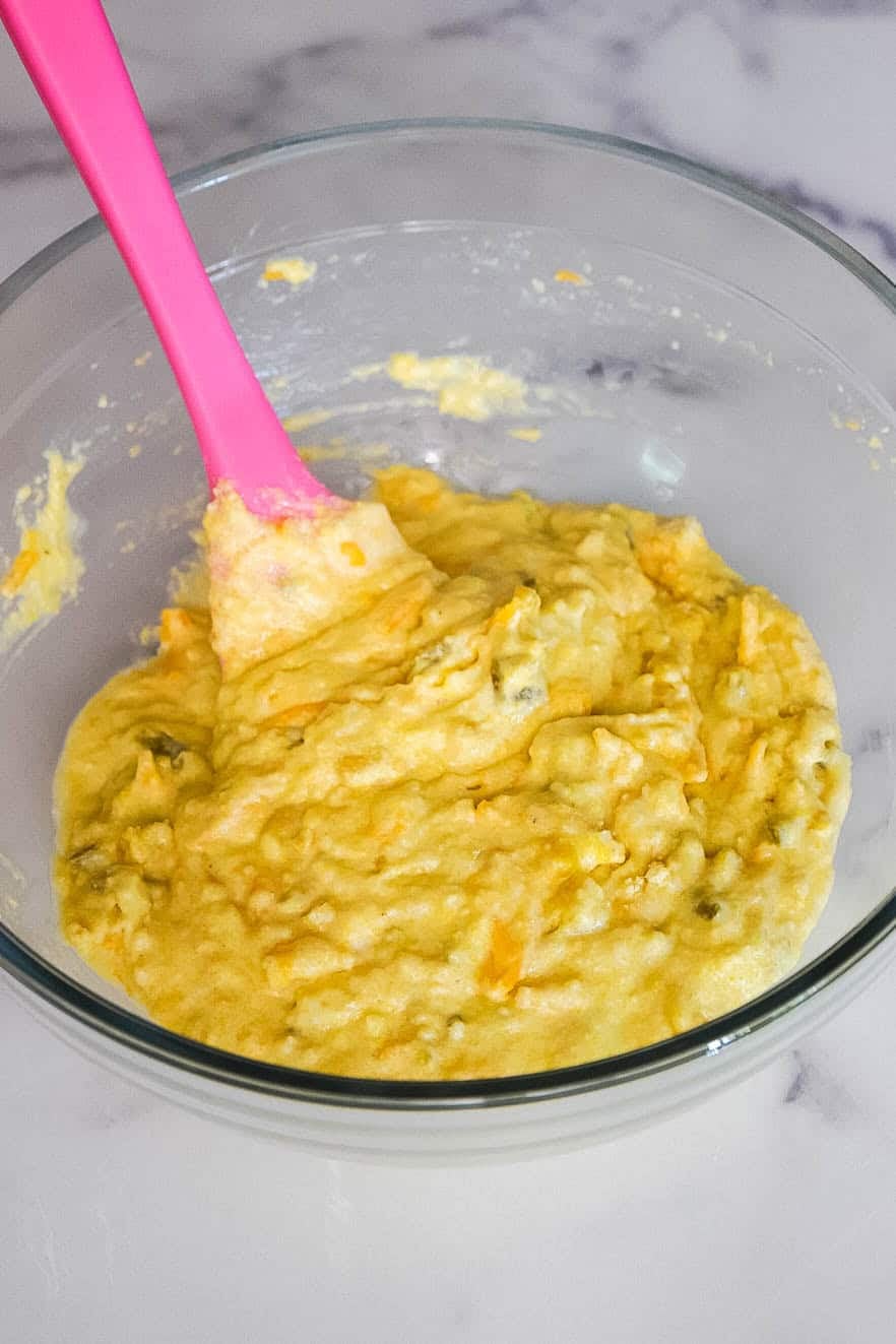 A glass bowl with thick jiffy jalapeño cornbread muffin batter being mixed with a spatula.