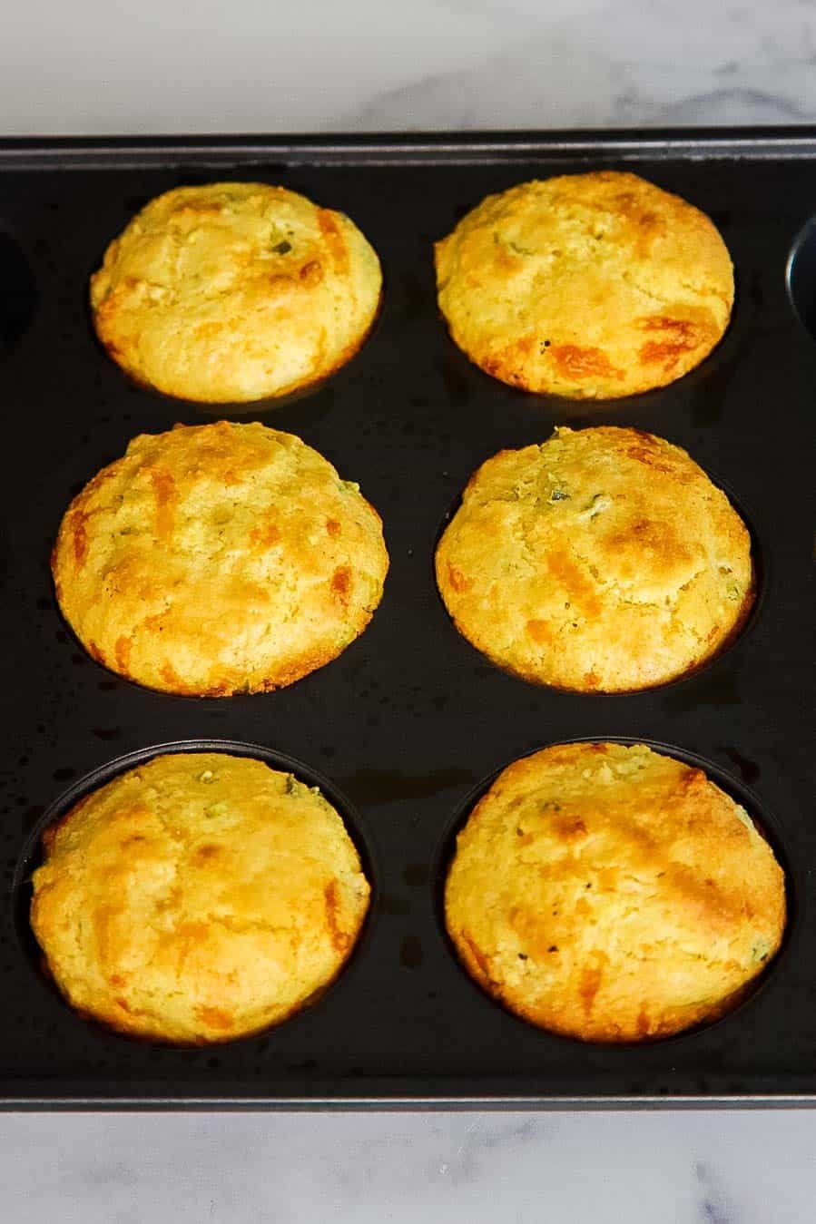 Freshly baked jiffy jalapeño cornbread muffins still in the muffin tin with golden domed tops.