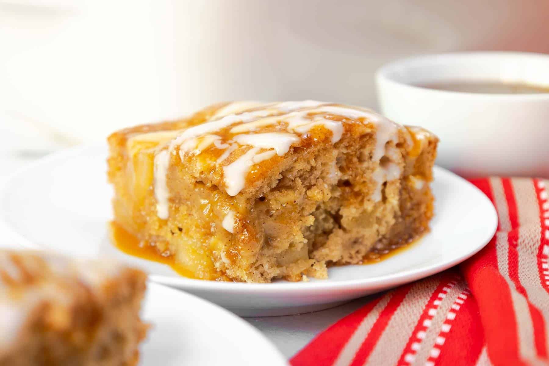 A generous slice of apple cake with visible apple chunks, topped with glaze and caramel.