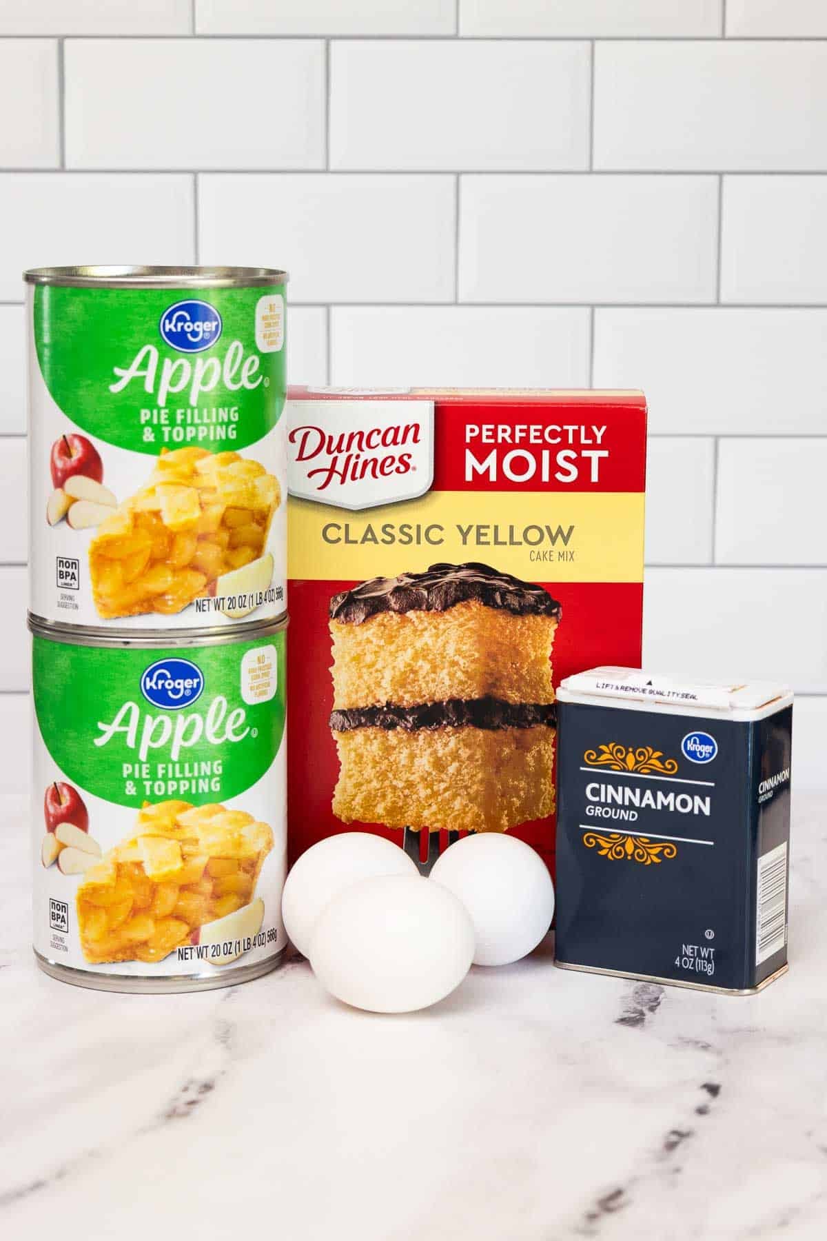 Ingredients for apple cake including canned apple pie filling, classic yellow cake mix, ground cinnamon, and three eggs.