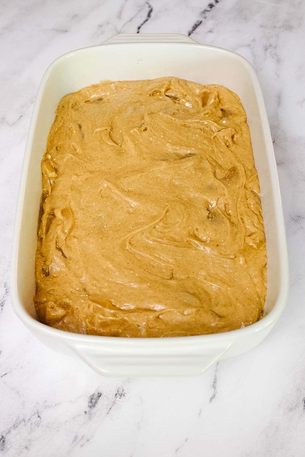 Unbaked apple cake batter spread evenly in a 9 by 13 inch baking dish, ready for the oven.