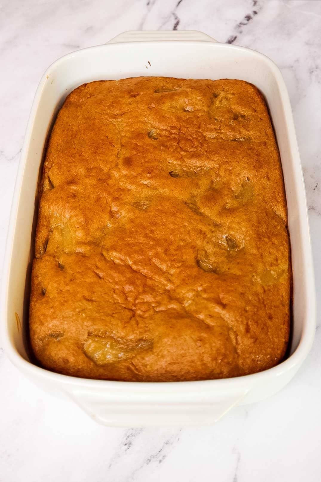 Freshly baked apple cake made with cake mix shown just out of the oven with a golden-brown top and visible apple chunks.