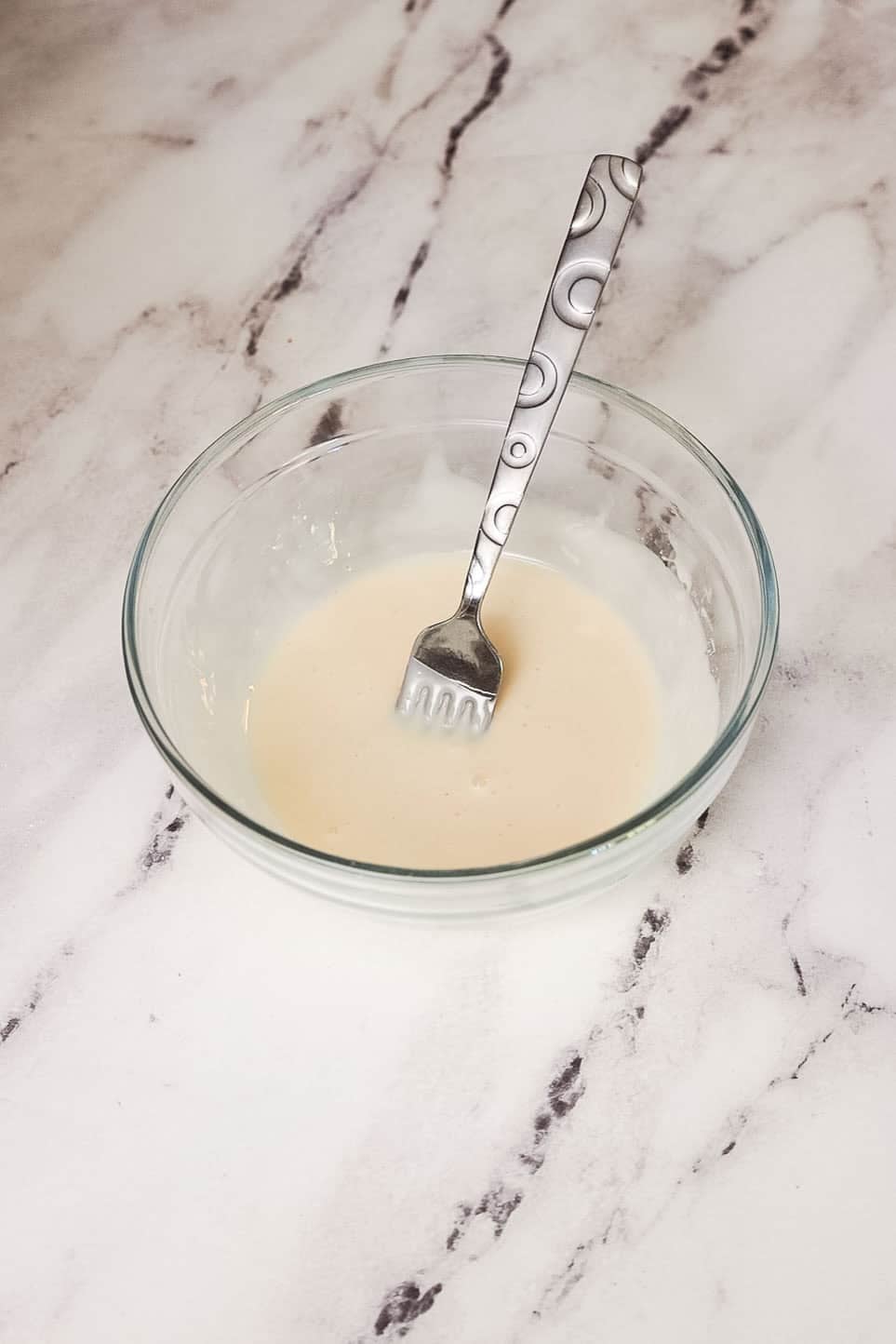 A small glass bowl of vanilla glaze with a fork.