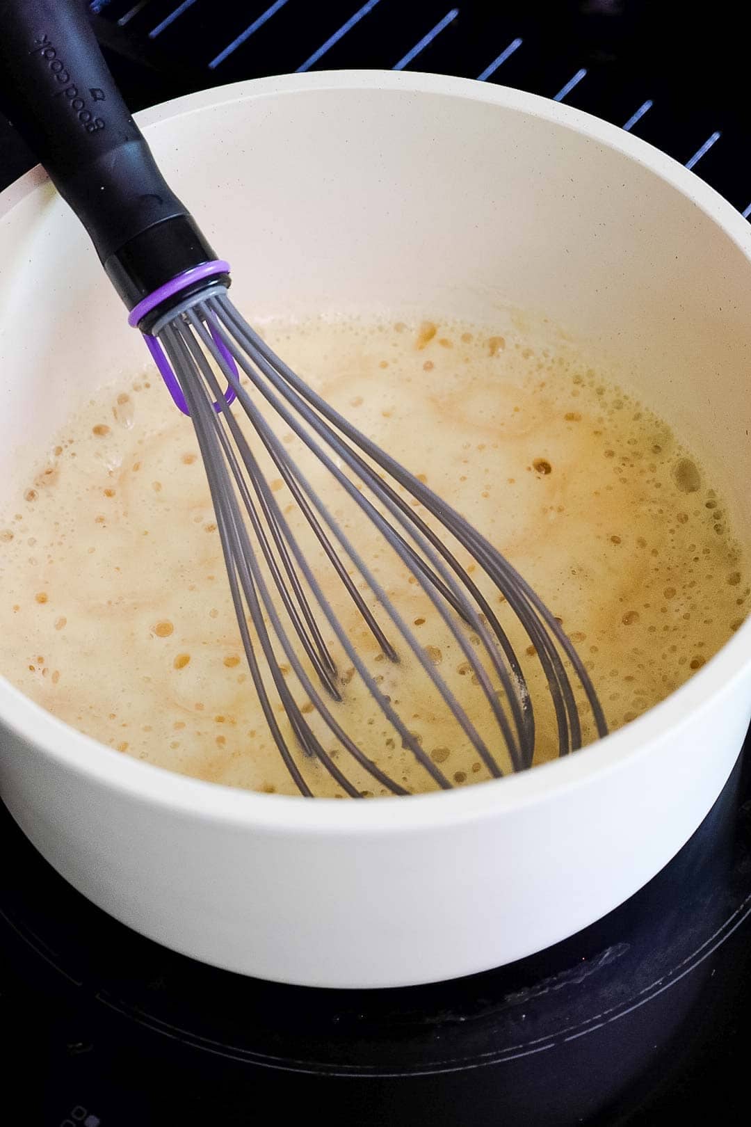 A saucepan with a bubbling roux being whisked on a stovetop as the base for the cheese sauce.