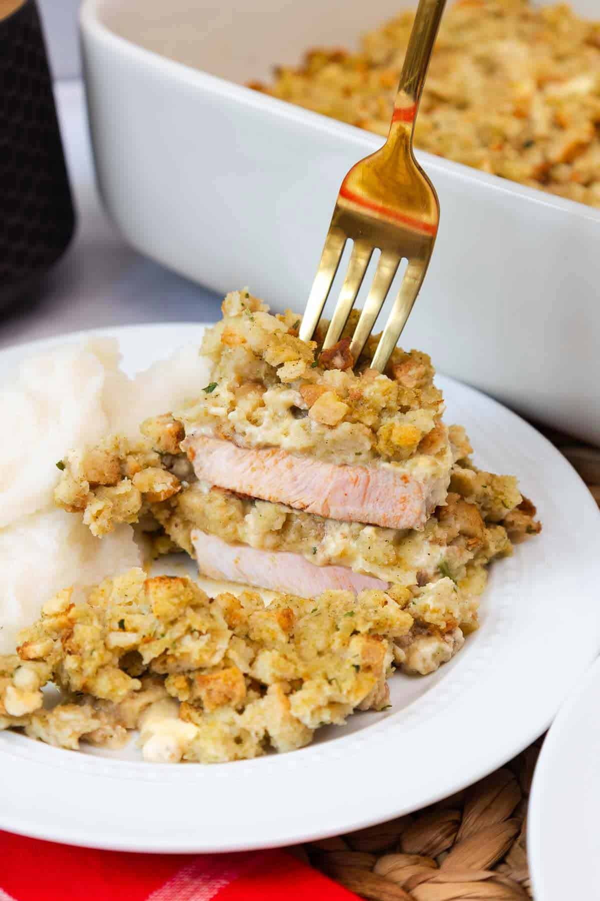 A close-up view of sliced pork chops topped with stuffing, showing the juicy meat and creamy filling beneath the crispy topping.
