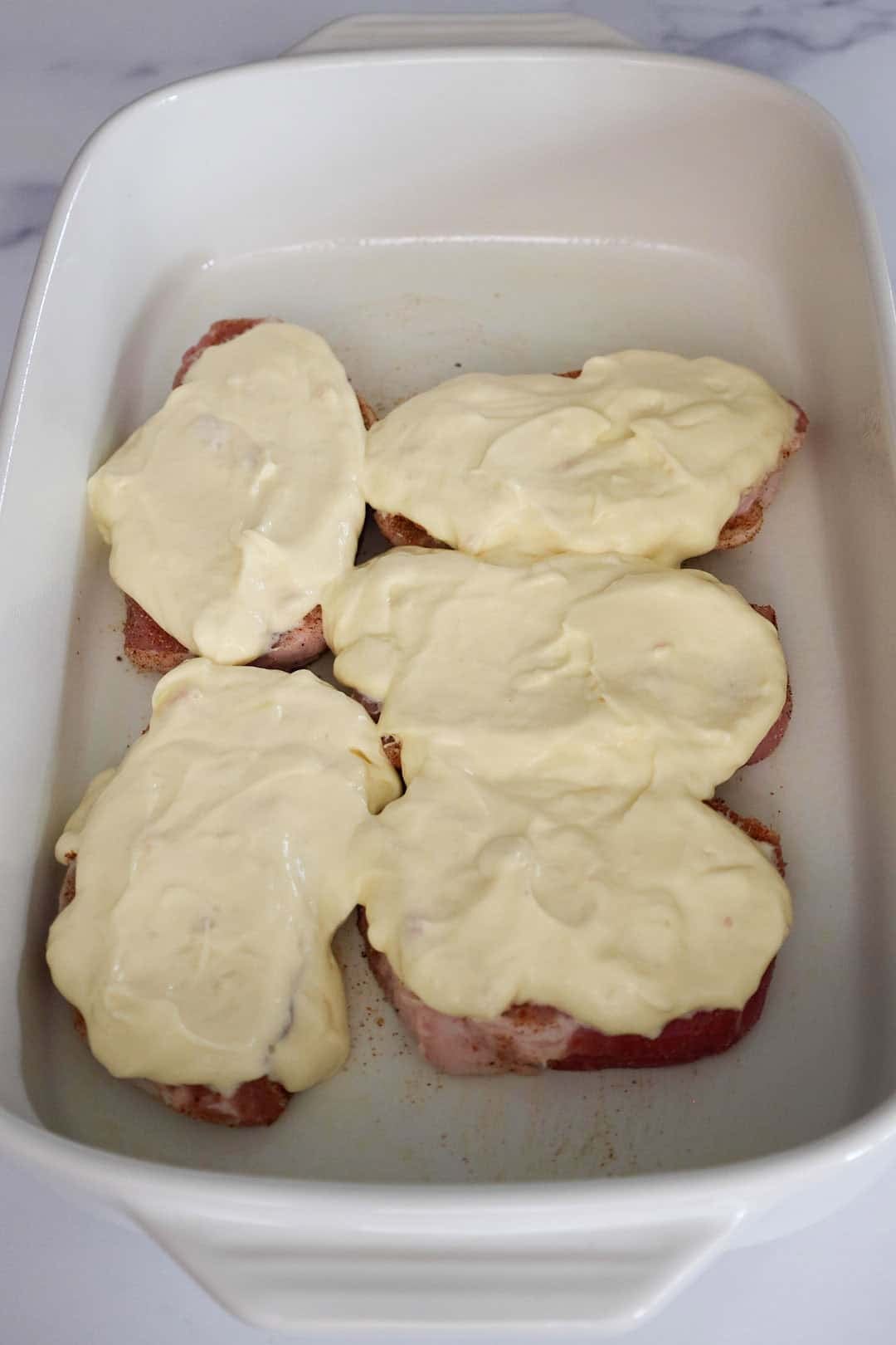 Pork chops in a baking dish topped with a thick layer of creamy mixture made from soup and sour cream.