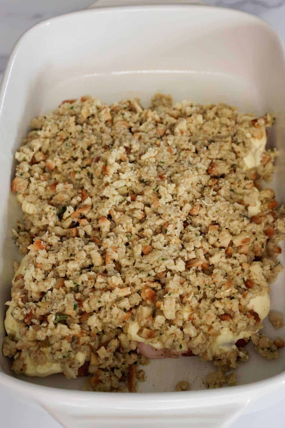 The baking dish now covered with a layer of stuffing over the creamy pork chops, ready to be covered in foil and baked.