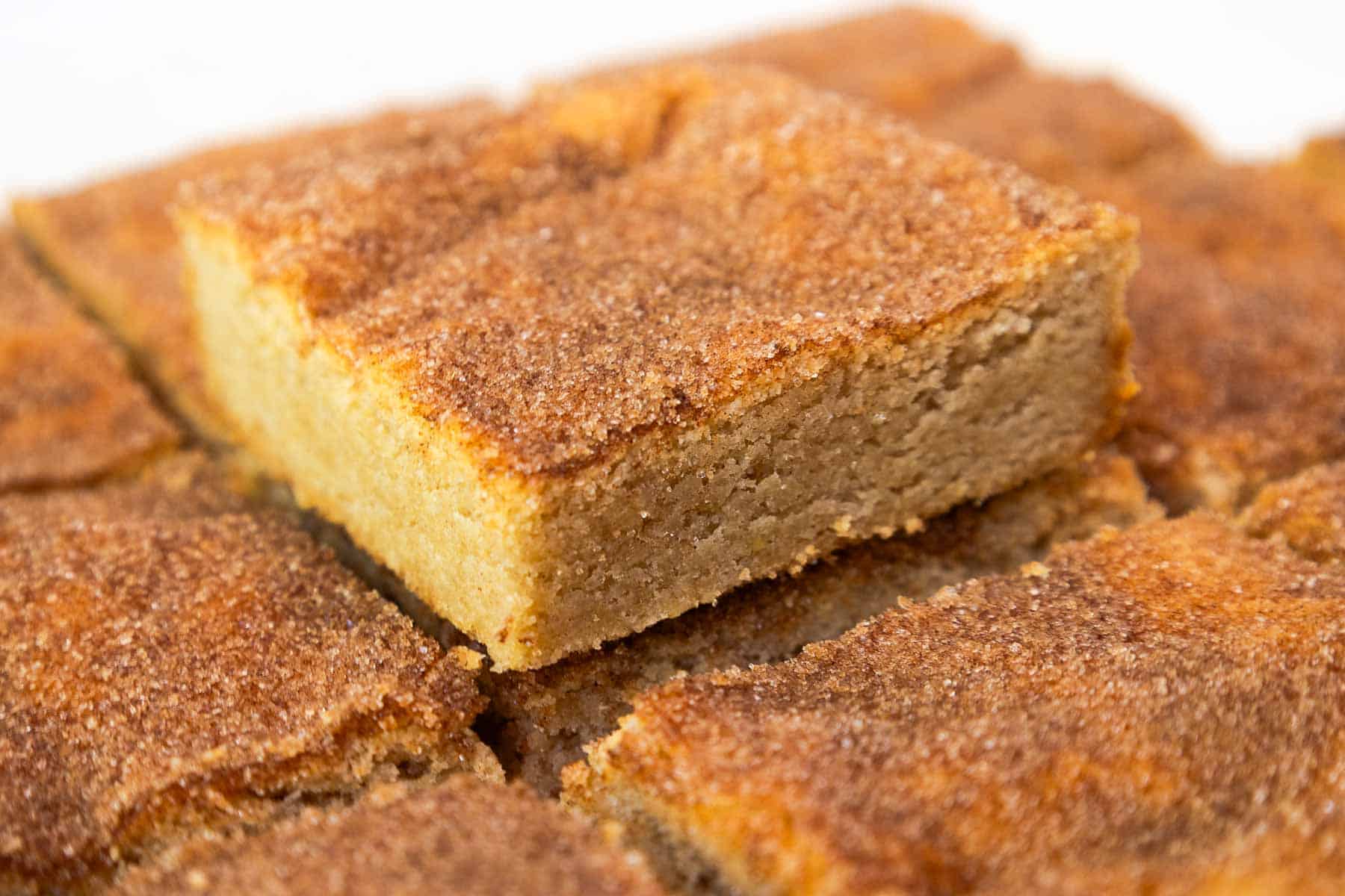 A snickerdoodle cookie bar stacked on top of a layer of cookie bars, showing its soft, dense texture and cinnamon-sugar topping.