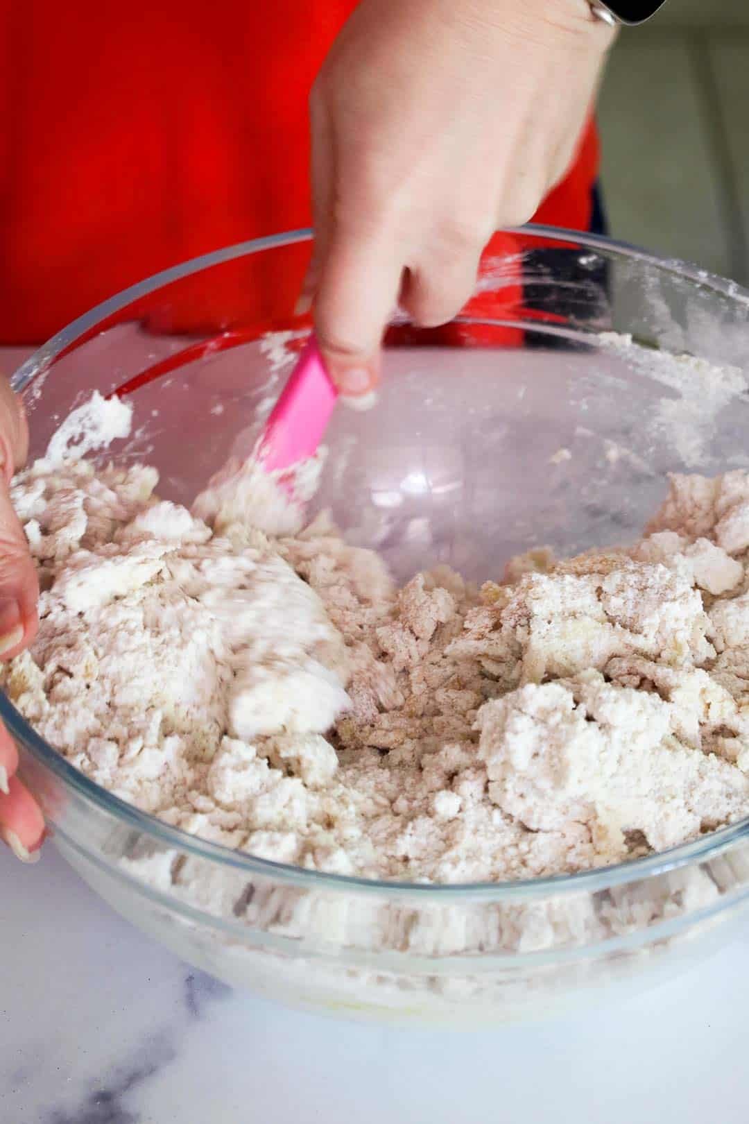 Cookie dough being mixed in a large mixing bowl until the dough has a shaggy texture.